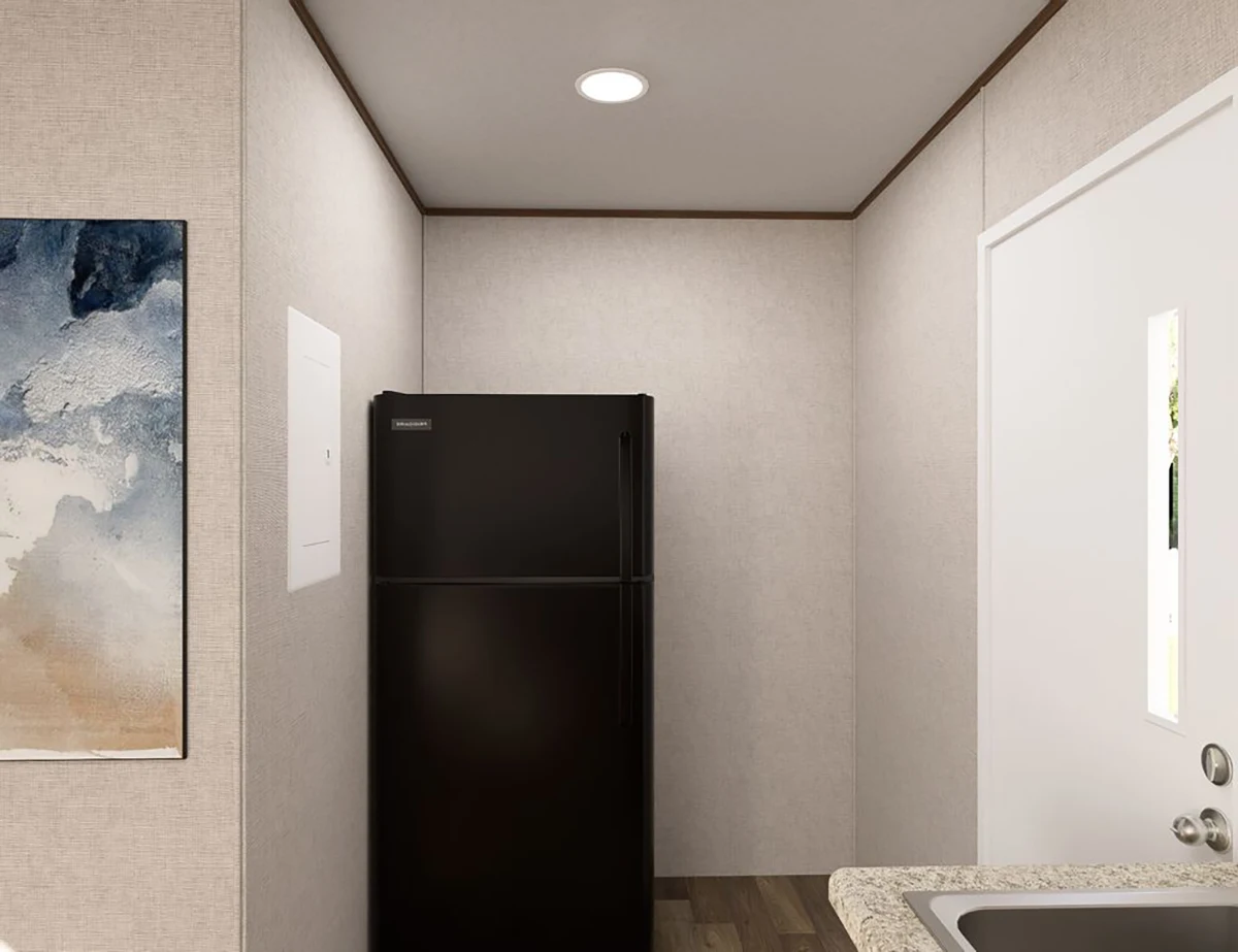 A black refrigerator stands against the back wall of a narrow room with light-colored walls, a door on the right, and part of a countertop and abstract painting visible.