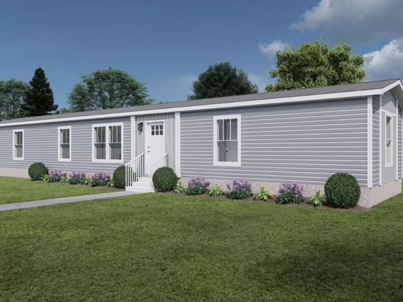 A single-story, light gray manufactured home with white trim, small front porch, and landscaping, situated on a grassy lawn with a white fence and trees in the background.