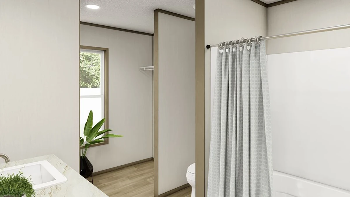 Bathroom with light-colored walls, a bathtub with a gray shower curtain, a sink with a countertop, a plant near a window, and a toilet partially visible behind a partition.