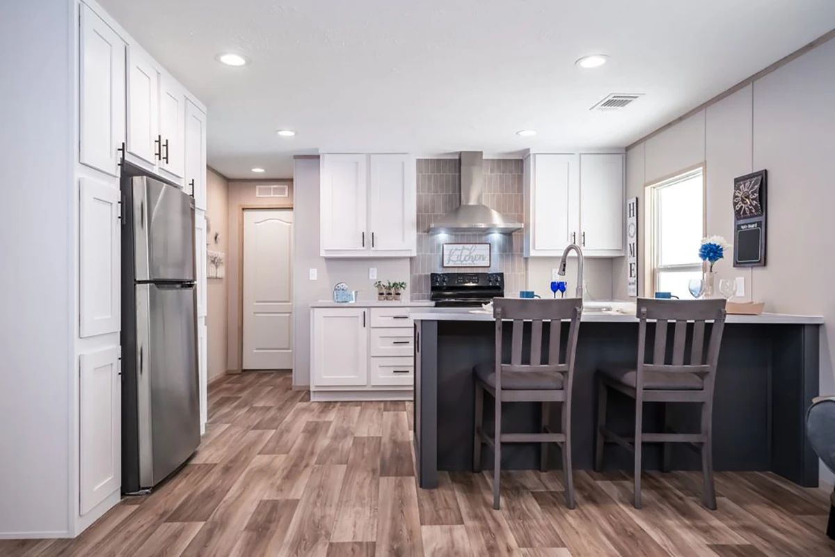 Modern kitchen with stainless steel appliances, white cabinets, island with sink and two chairs, wood-style flooring, and bright lighting.