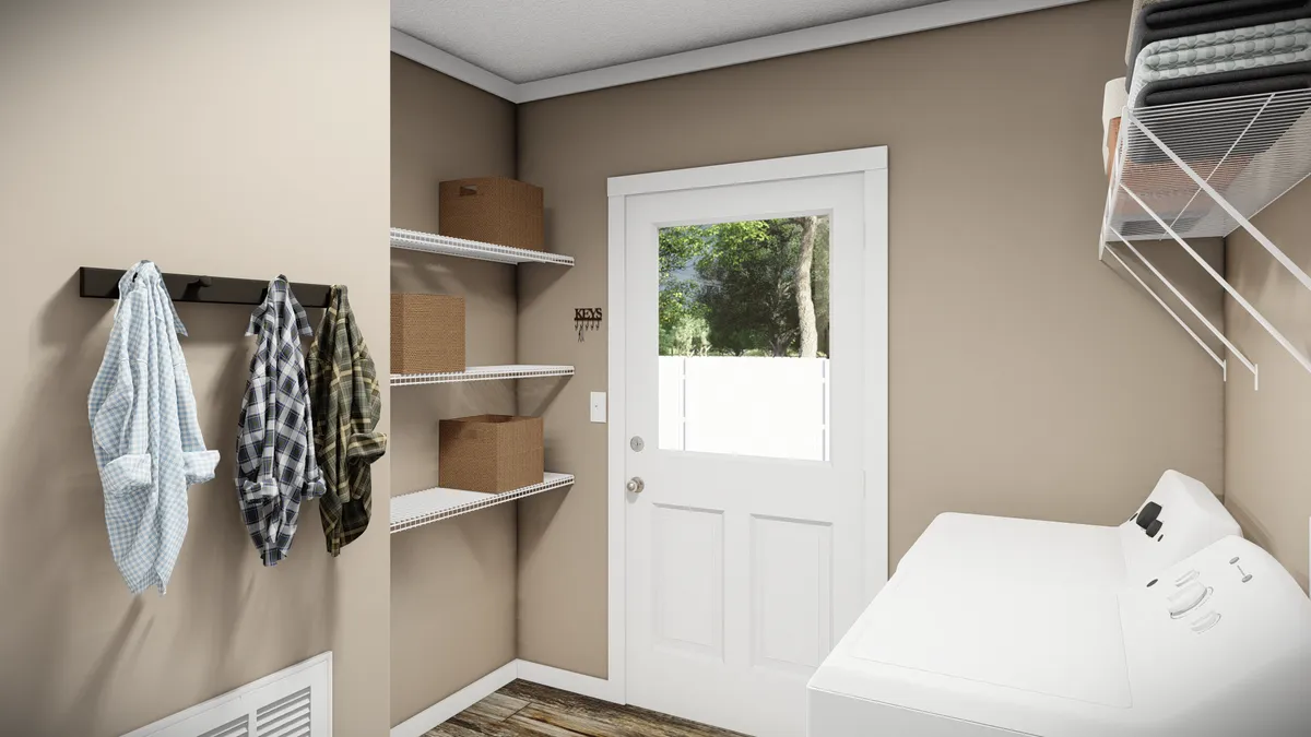 A laundry room with a washer, wall shelves holding boxes, clothes hanging on hooks, and a white door with a window leading outside.