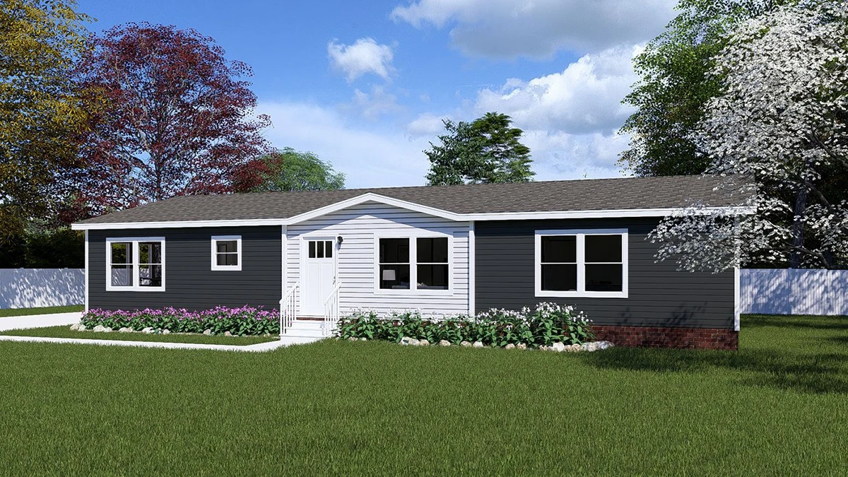 Single-story house with dark siding, white trim, and a gabled entrance. Surrounded by a green lawn, white flowers, and trees under a partly cloudy sky.