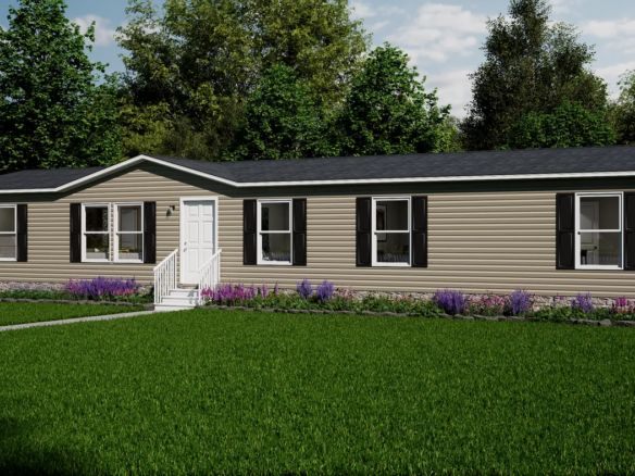 A single-story beige manufactured home with black shutters, white trim, and a small porch is set on a green lawn with purple flowers and trees in the background.
