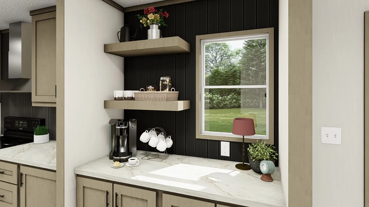 A kitchen counter with a coffee maker, cups on hooks, shelves with decor and baskets, a window with a view of greenery, and a small lamp on the countertop.