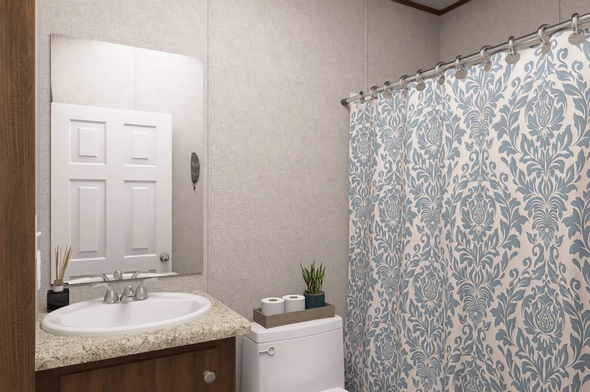 16ebaf63-20ba-4011-80ce-b09e644931d8 Bathroom with a sink, mirror, toilet, and a blue floral shower curtain. A small plant and toilet paper sit on the toilet tank. Neutral wall color and granite countertop.