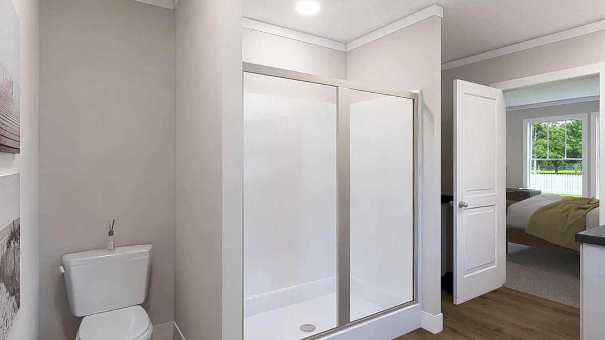 Bathroom with a white toilet, a glass-enclosed shower, light-colored walls, and wood flooring. An open door leads to a bedroom with a bed and window.