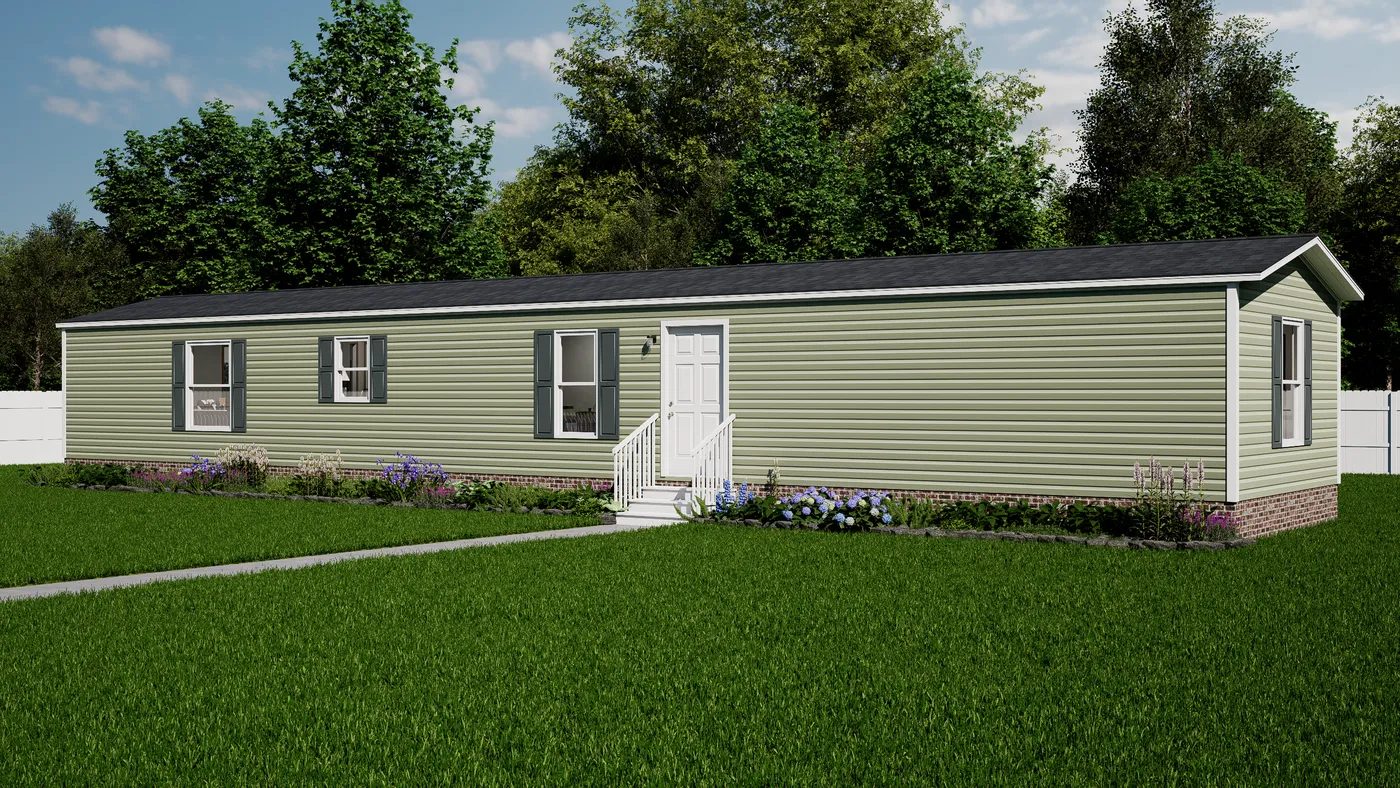 A single-story, light green manufactured home with white trim, small steps leading to the front door, and a well-kept lawn bordered by shrubs and flowers, set against a backdrop of trees.