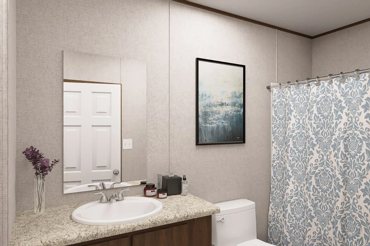 1acfa20f-7f67-4de5-8593-01bca510d6a3 Bathroom with a granite countertop, sink, mirror, wall art, toilet, tissue box, and a blue patterned shower curtain. A vase with purple flowers sits by the sink.