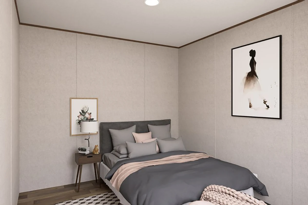 A neatly made bed with gray and beige bedding sits in a corner bedroom; a nightstand with a lamp and artwork are on one side, and framed art decorates the walls.