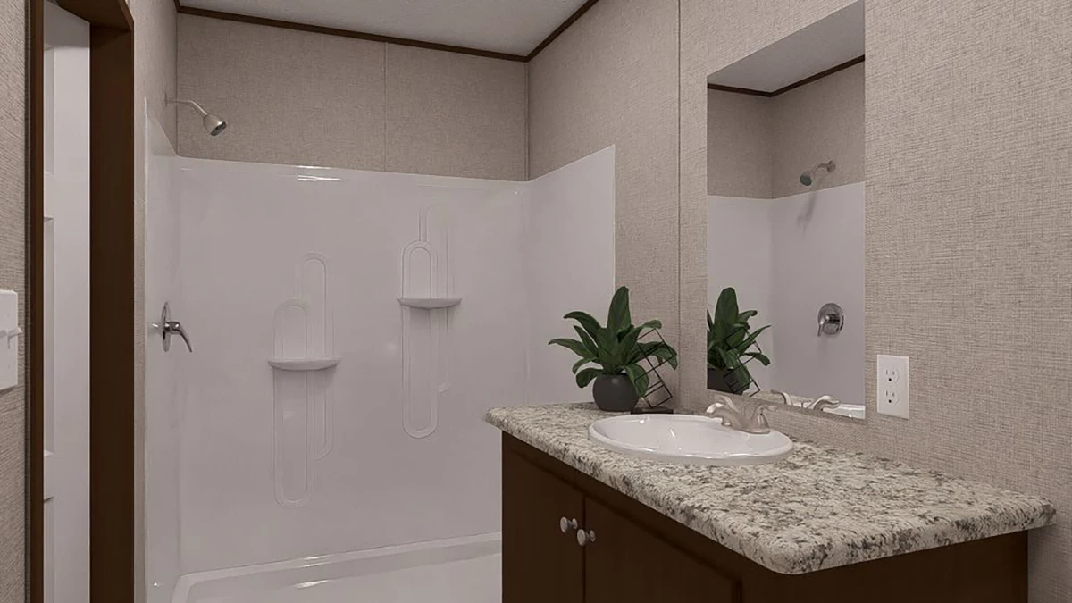 A bathroom with a walk-in shower, a granite countertop vanity with a sink, two potted plants, and a wall mirror above the sink.