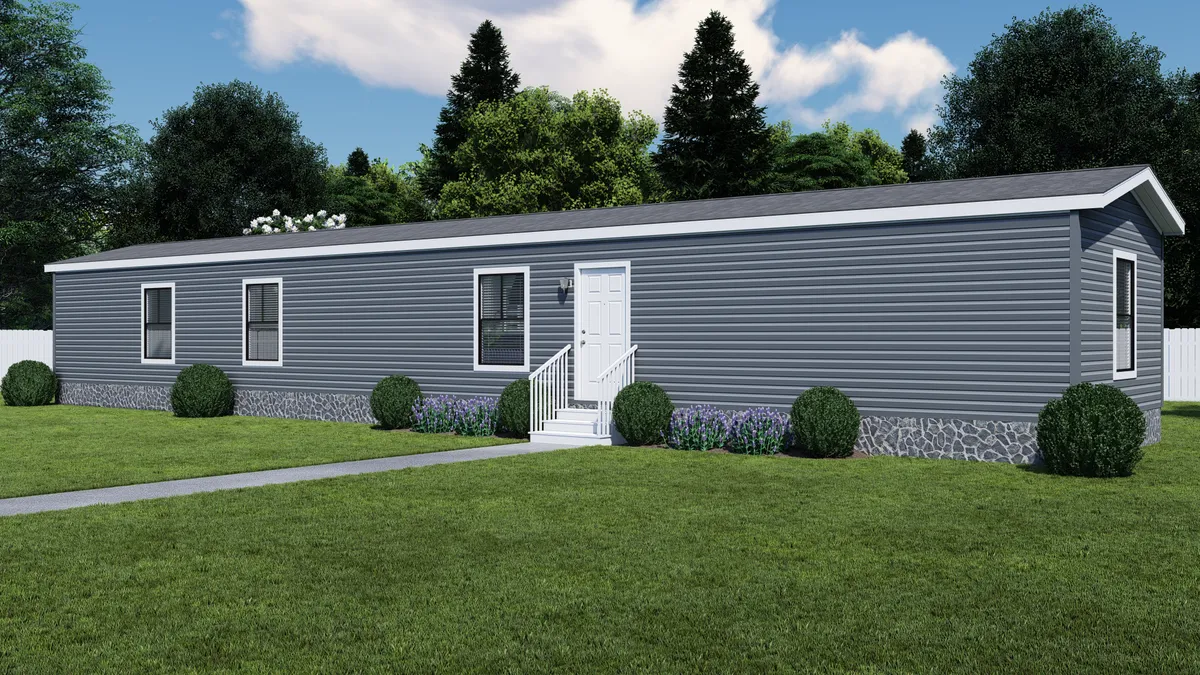 1f46e40d-3f3a-4aea-a952-1108441a2069 A gray single-wide manufactured home with white trim, front door with steps, and small shrubs in front, set on a green lawn with trees in the background.