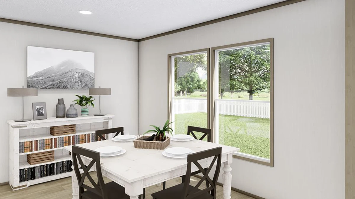 A bright dining area with a white table set for four, dark chairs, large windows, and a sideboard with books, decor, and a mountain photo on the wall.