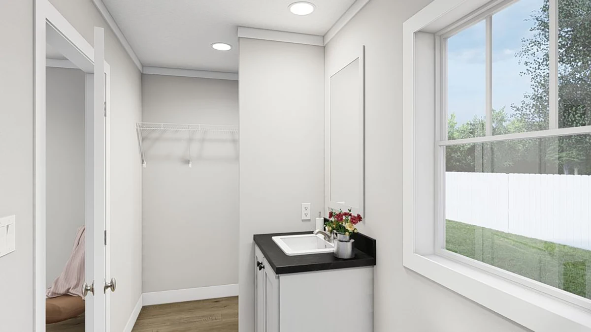 A small laundry room with a countertop sink, a potted plant, a wire shelf on the wall, and a large window overlooking a fenced yard.