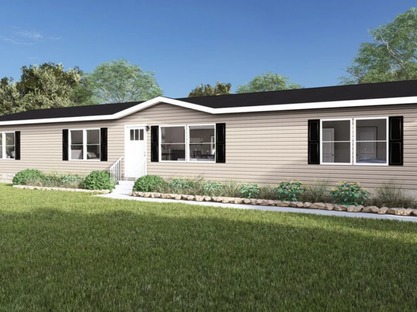 A beige single-story manufactured home with black shutters, white trim, and a small front porch, set on a grassy lawn with shrubs and a white fence in the background.