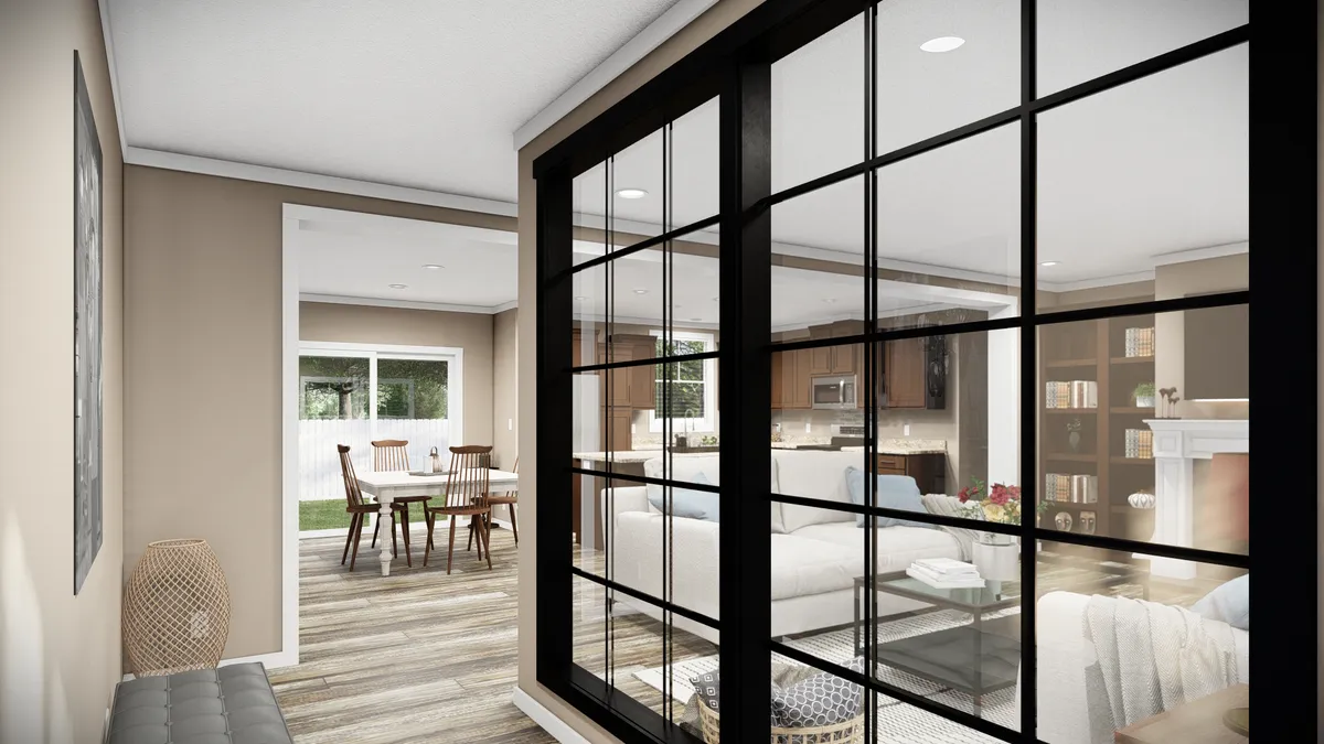 A modern open-concept living space viewed through black-framed glass doors, showing a living room, dining area, and kitchen with neutral decor and wood flooring.