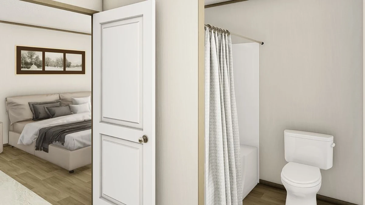 A bedroom with a bed and wall art is adjacent to a bathroom featuring a toilet and a shower with a curtain, separated by a partial wall and an open door.