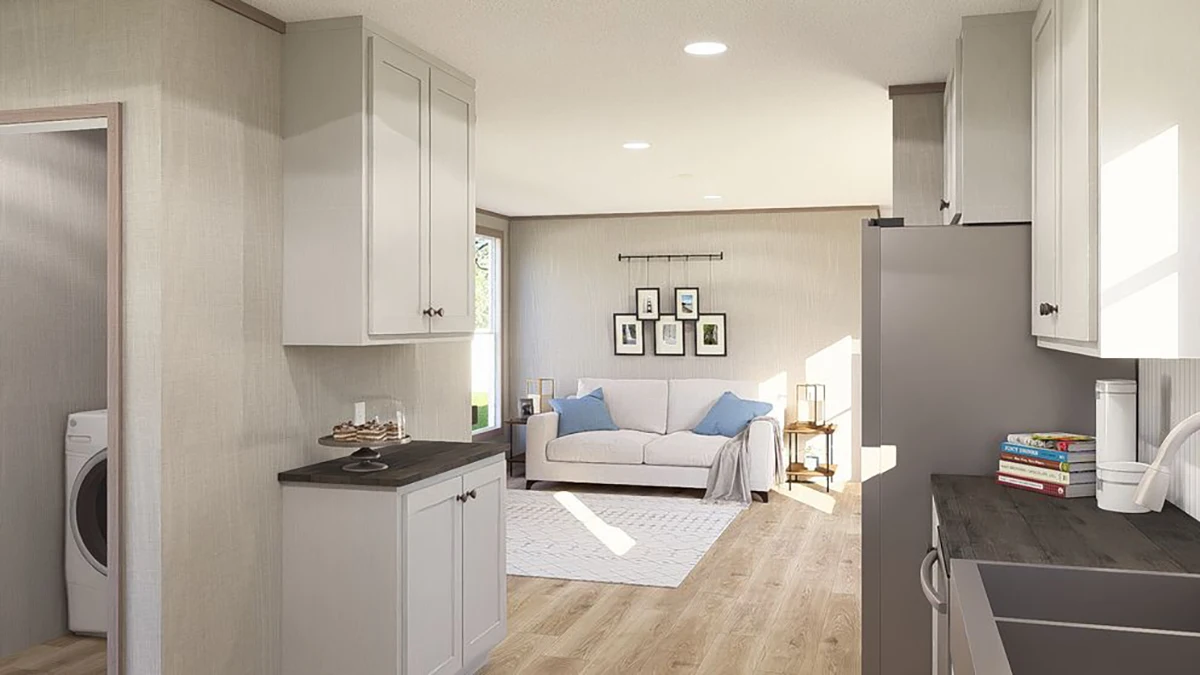 27da5518-1dd9-467b-9483-05598cc92e48 Modern open-concept kitchen and living room with light wood floors, white cabinets, a gray sofa, and a visible laundry area through an open doorway.