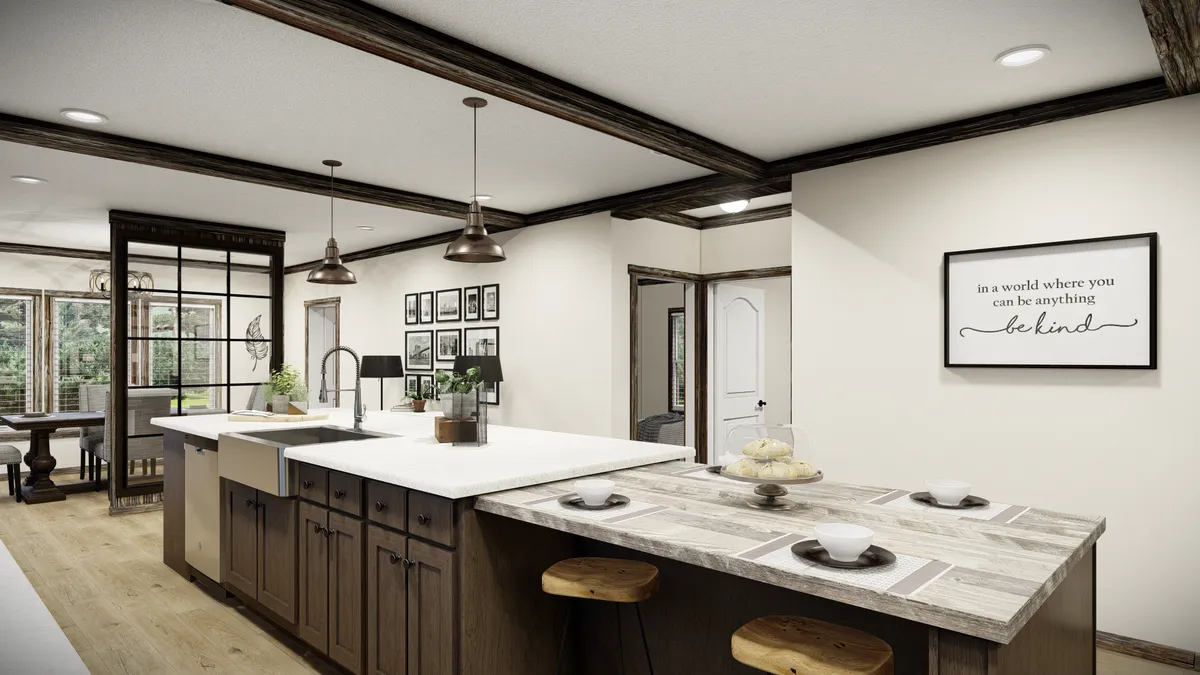 2a83f7bf-04ad-4352-8f9f-dfe7cc3aa7f6 Modern kitchen with a large island, farmhouse sink, pendant lights, bar stools, and wall decor including a framed quote; adjacent dining area visible in the background.