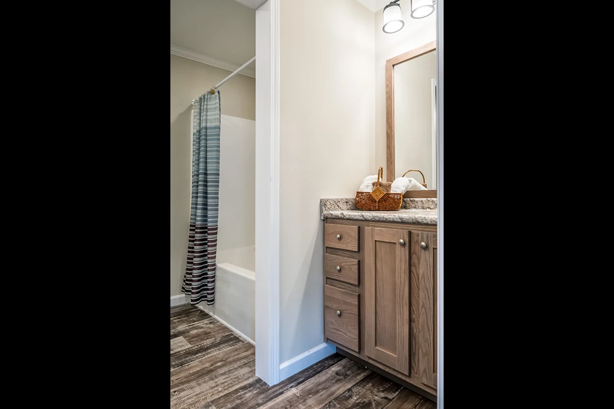 Bathroom with wood-look flooring, a vanity with a granite countertop, a wall mirror, and a shower-tub combo with a striped curtain.