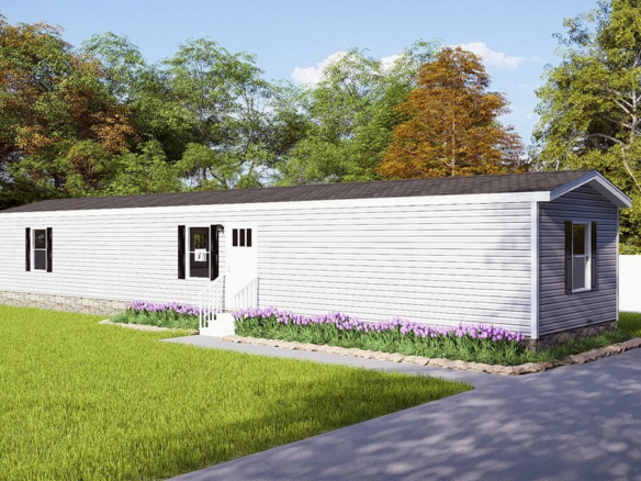 A single-wide manufactured home with gray siding, a small front porch, and a paved driveway, surrounded by a grassy yard and trees.