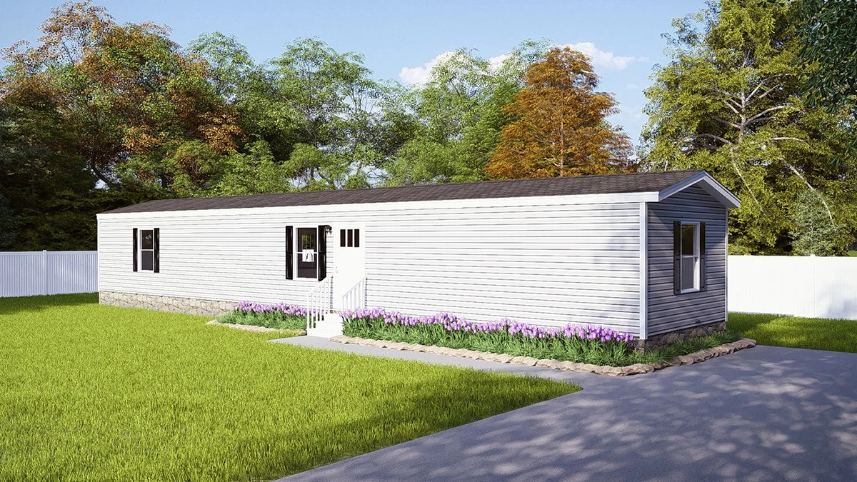 A single-wide manufactured home with gray siding, a small front porch, and a paved driveway, surrounded by a grassy yard and trees.