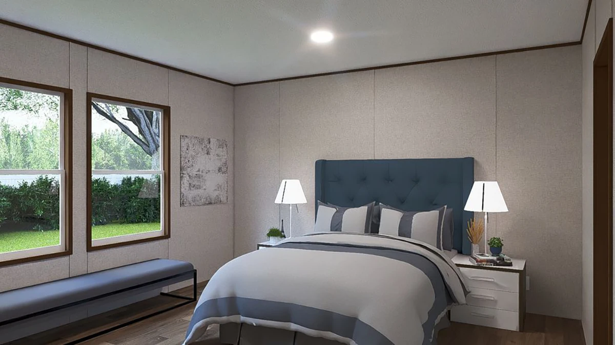 A modern bedroom with a blue upholstered bed, two bedside tables with lamps, a bench under two windows, and greenery visible outside.