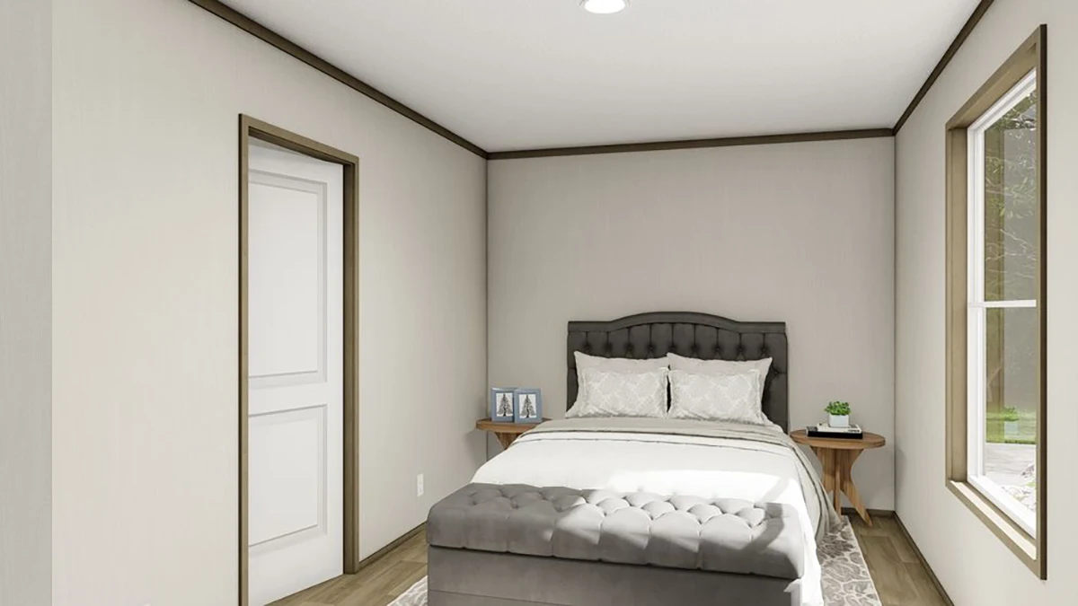 3453199b-c67d-406e-8608-77d2f534f6b9 A small bedroom with a bed, gray upholstered headboard, bench at the foot, two side tables with framed photos and a plant, and a window letting in natural light.