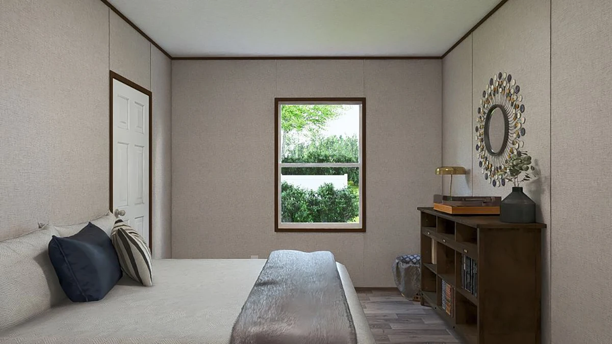 A simple bedroom with a neatly made bed, a window showing greenery outside, a wooden bookshelf with decor, and a round mirror on the wall.
