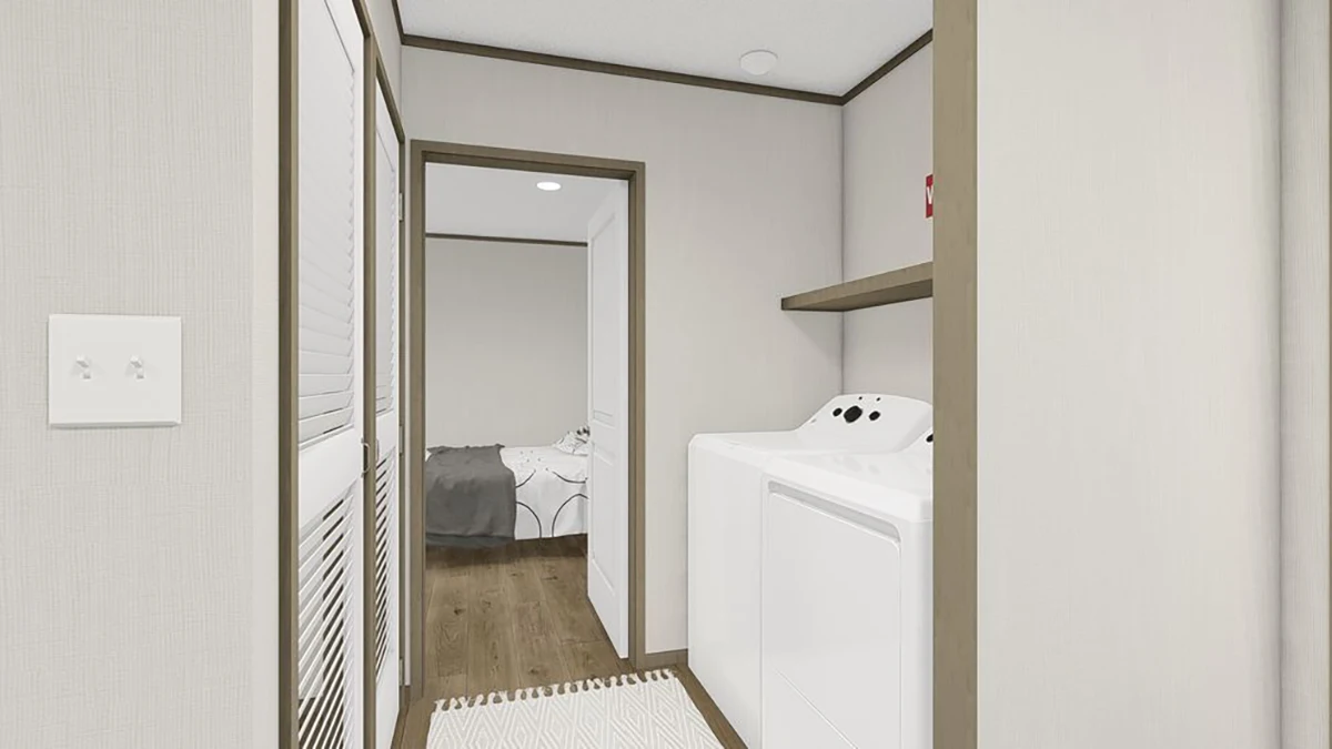 A laundry area with a washing machine and dryer, open shelf above, and a view into a bedroom with a bed and patterned bedding.