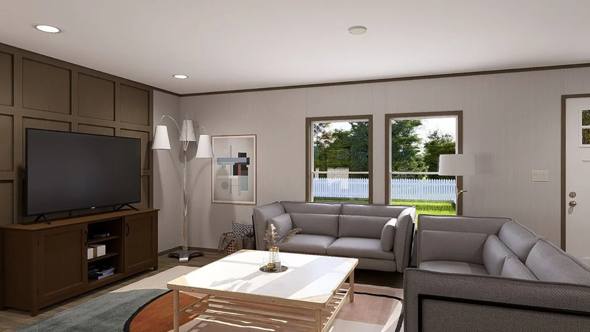 Modern living room with two gray sofas, a TV on a cabinet, a white coffee table, floor lamps, framed wall art, and large windows showing a yard with green grass and a white fence.