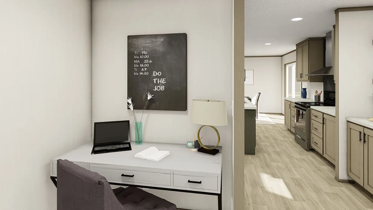 A small workspace with a laptop, lamp, books, and vase sits next to a kitchen area in a modern home with light wood flooring and neutral walls.