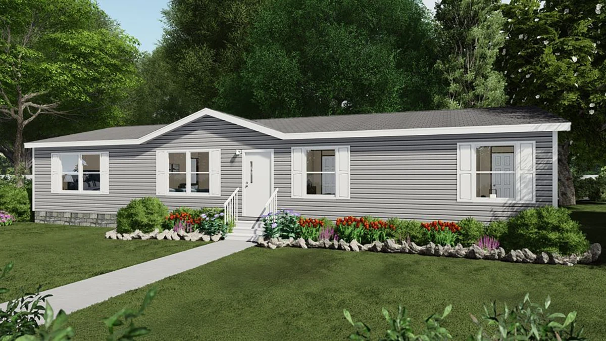 A single-story manufactured home with gray siding, white trim, and a small front porch, surrounded by a landscaped yard with flowers and shrubs.