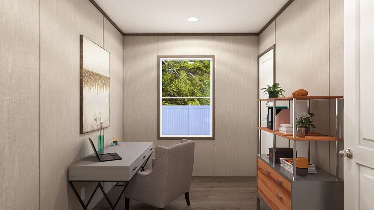 A small home office with a desk, chair, bookshelf, wall art, and a window with a view of green trees and a fence.