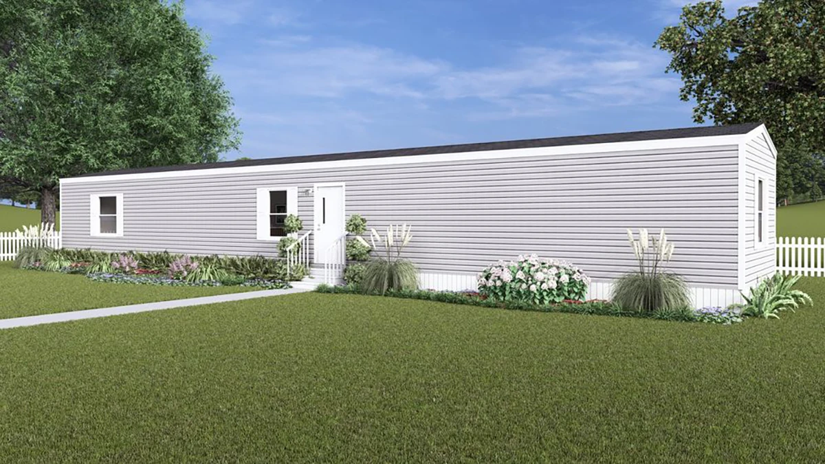 42f7d010-bbe2-453c-817b-bdea477049b7 A single-story manufactured home with light gray siding, white trim, and a small front garden, set on a grassy lawn with a white fence and trees in the background.