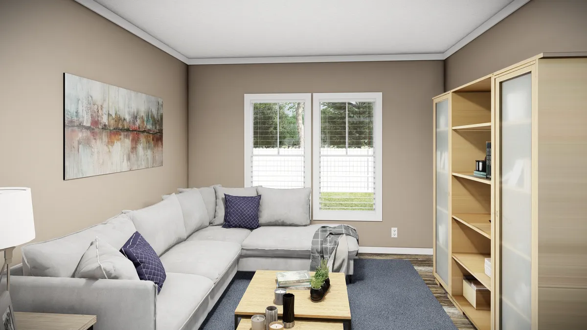 A living room with a gray sectional sofa, wooden bookshelf, coffee table, abstract wall art, and windows with white blinds.