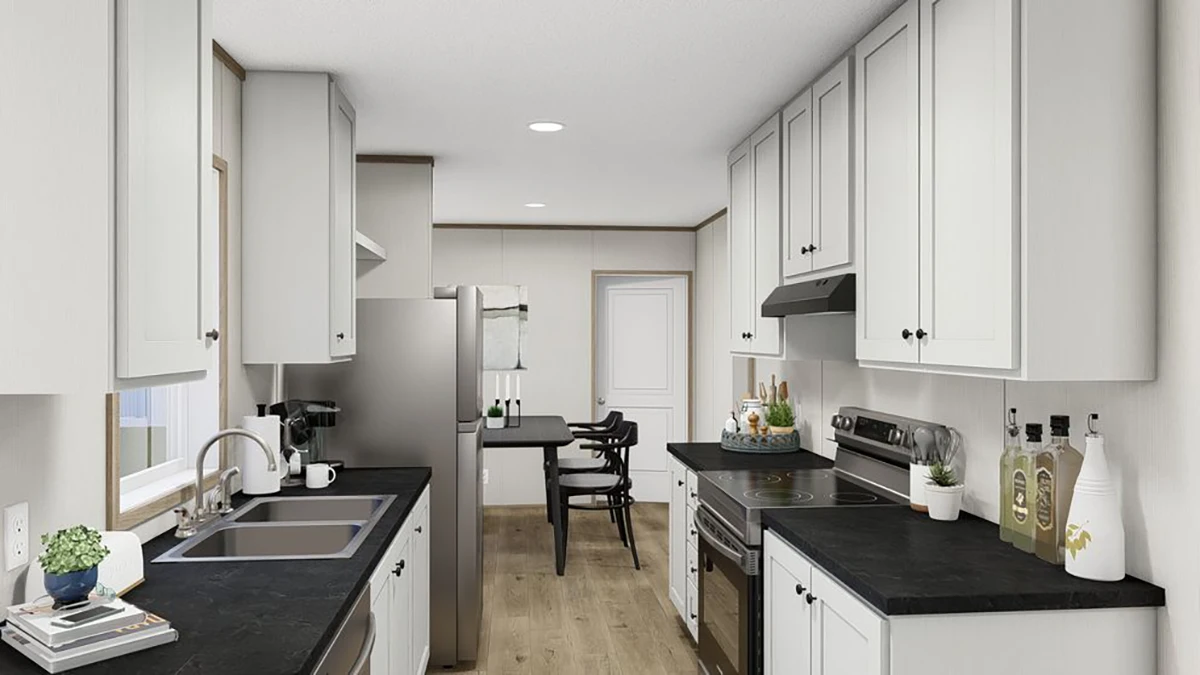 Modern kitchen with white cabinets, black countertops, stainless steel appliances, and a small dining area in the background. Light wood flooring and minimal decor are featured.