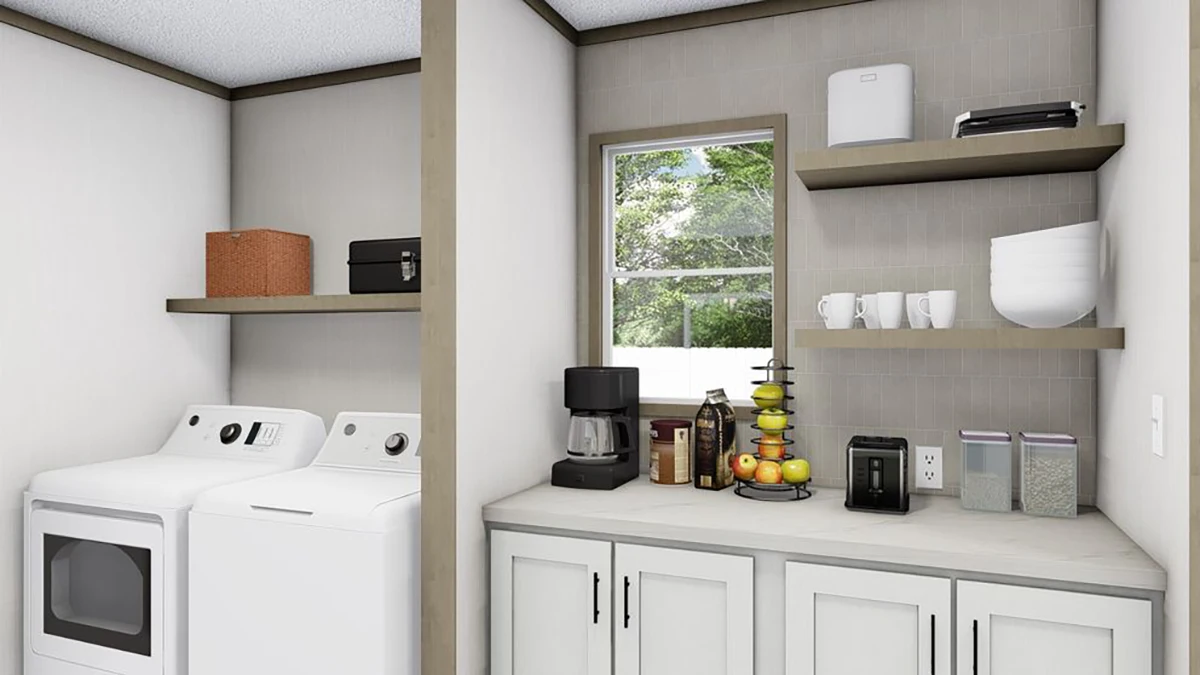 A laundry room with a washer, dryer, cabinets, countertop appliances, shelves with boxes and mugs, and a window showing greenery outside.