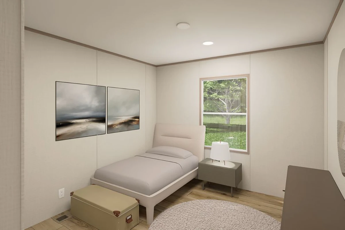 A small, minimalist bedroom with a single bed, a nightstand with a lamp, artwork on the wall, a suitcase at the foot of the bed, and a window showing greenery outside.
