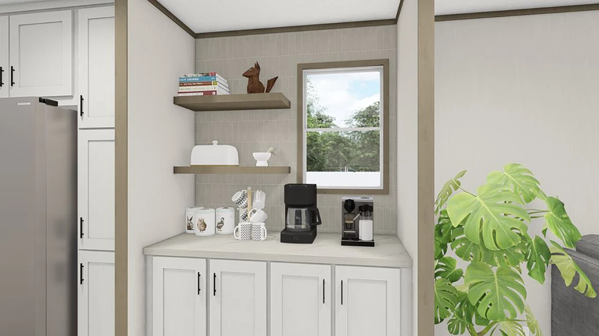 A kitchen nook with white cabinets, a coffee maker, mugs, a bread box, two wooden shelves with books and decor, and a window above the counter. A green plant is on the right.