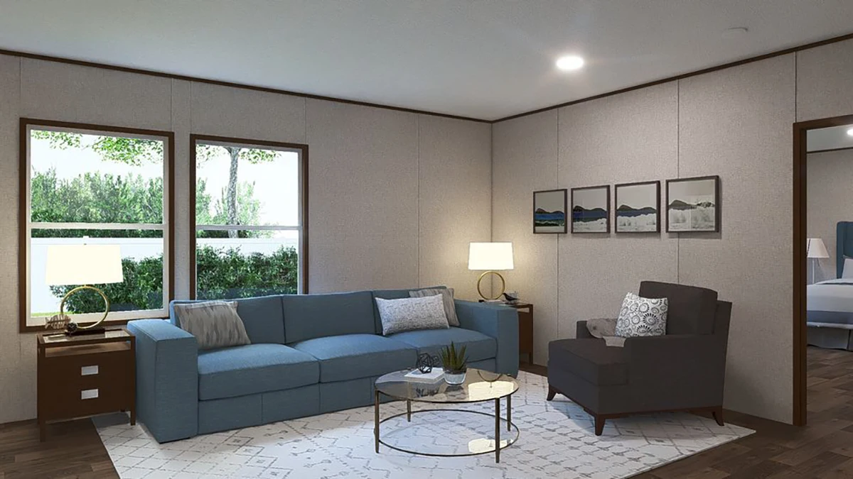 A living room with a blue sofa, gray armchair, round glass coffee table, two lamps, wall art, and large windows overlooking greenery.