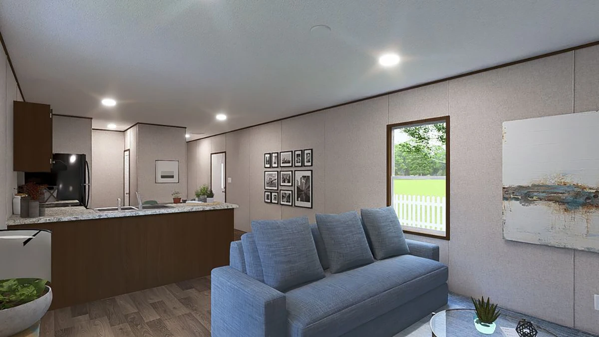 A modern living room with a blue sofa, a coffee table, and wall art. The adjoining kitchen features wood cabinets and a granite countertop. A window shows a view of a green yard and white fence.