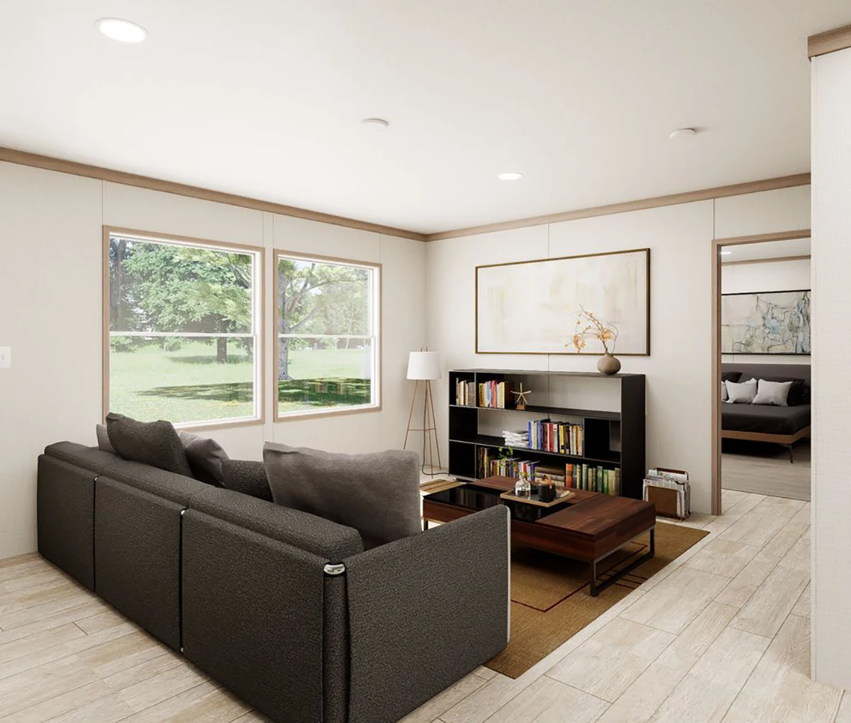Modern living room with a dark gray sectional sofa, bookshelf, coffee table, floor lamp, and large windows overlooking a green yard. Neutral color palette and minimal decor.