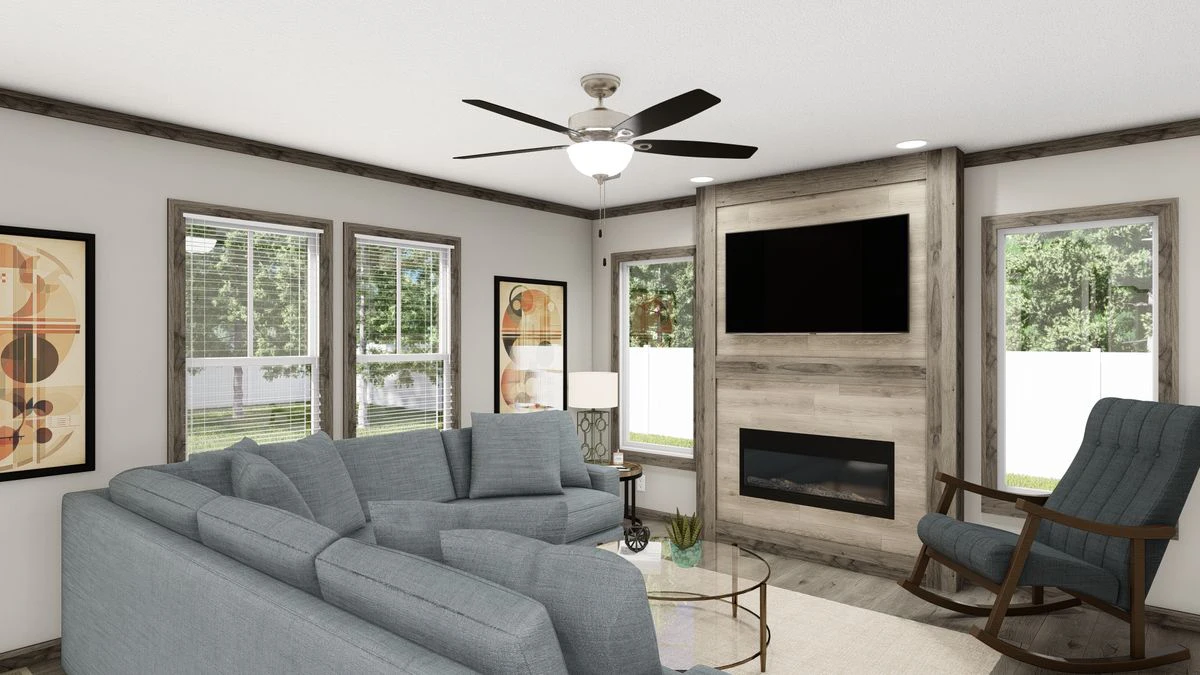 A modern living room with a gray sectional sofa, rocking chair, wall-mounted TV above a fireplace, large windows, and abstract artwork on the walls.