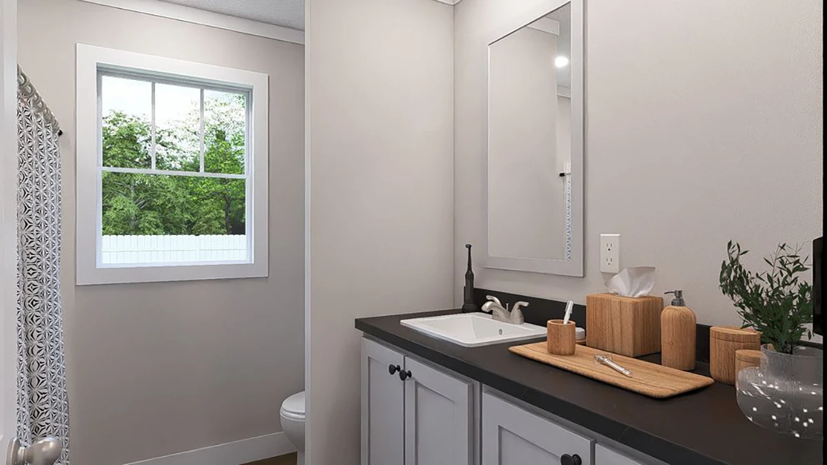 A modern bathroom with a black countertop, white sink, mirror, toiletries on a wooden tray, and a window showing greenery outside.