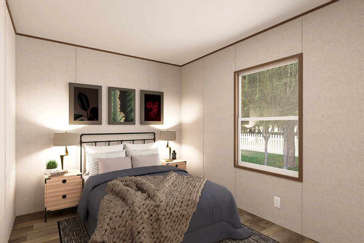 4f8428fd-3b11-4c2c-be00-bdfb05d98229 A neatly made bed with a gray blanket, two nightstands with lamps, three framed pictures above the headboard, and a window showing trees outside.