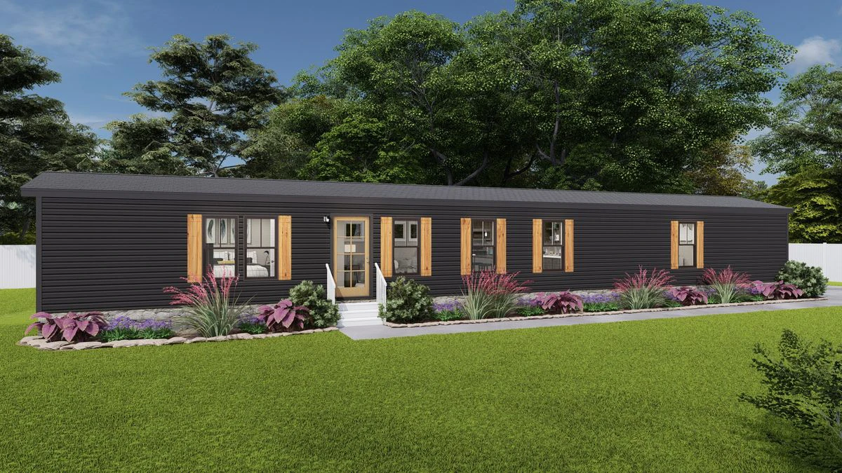Single-story modular home with dark siding, light wood shutters, and a landscaped front yard with shrubs and flowers, set against a backdrop of trees and grass.