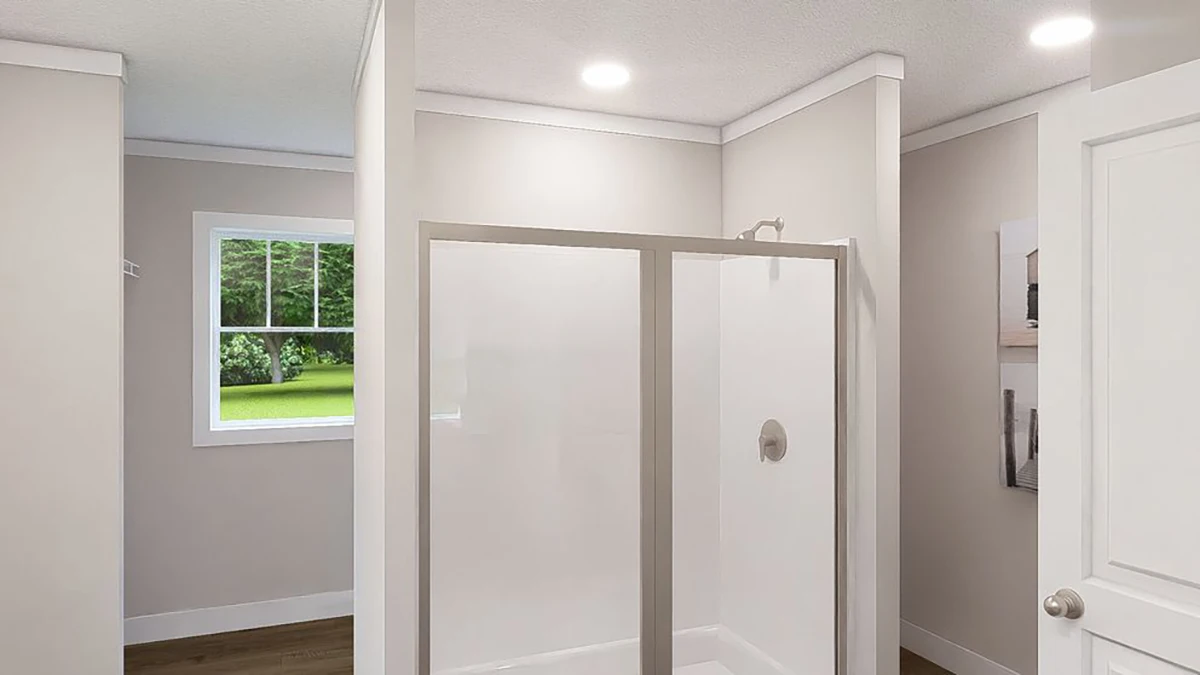 A modern bathroom with a glass-enclosed shower, beige walls, a white door, and a window showing greenery outside.
