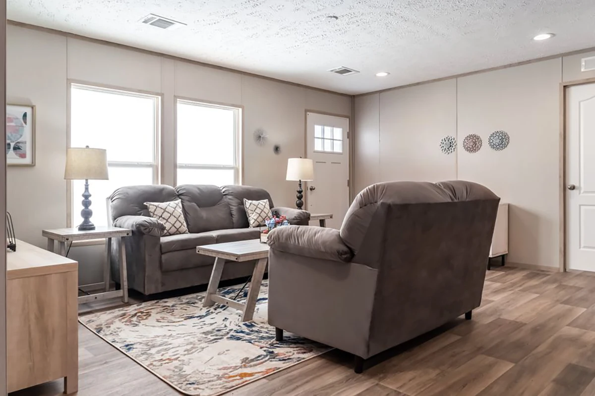 A living room with two gray sofas, a wooden coffee table, a patterned rug, two lamps, and wall decor on light-colored walls and wood flooring.