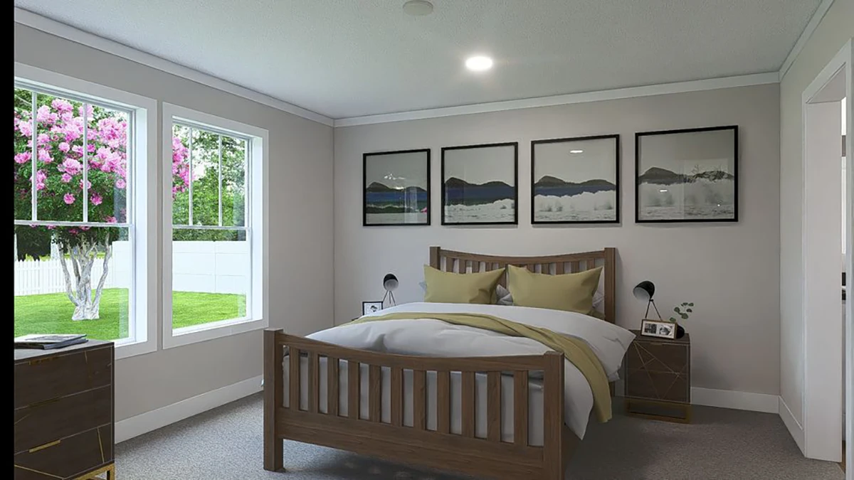 A bedroom with a wooden bed, yellow pillows, nightstands with lamps, four landscape pictures on the wall, and large windows showing a blooming tree outside.