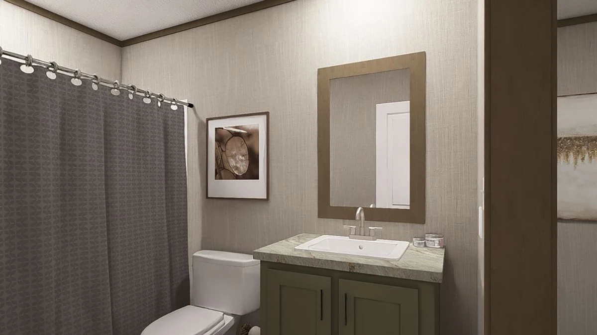 A bathroom features a shower with a gray curtain, a toilet, a sink with green cabinetry, a wall mirror, and framed artwork on beige walls.